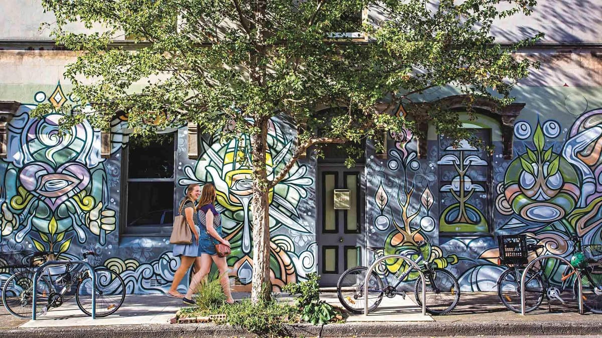 Cyclists passing a painted mural wall in the Inner West